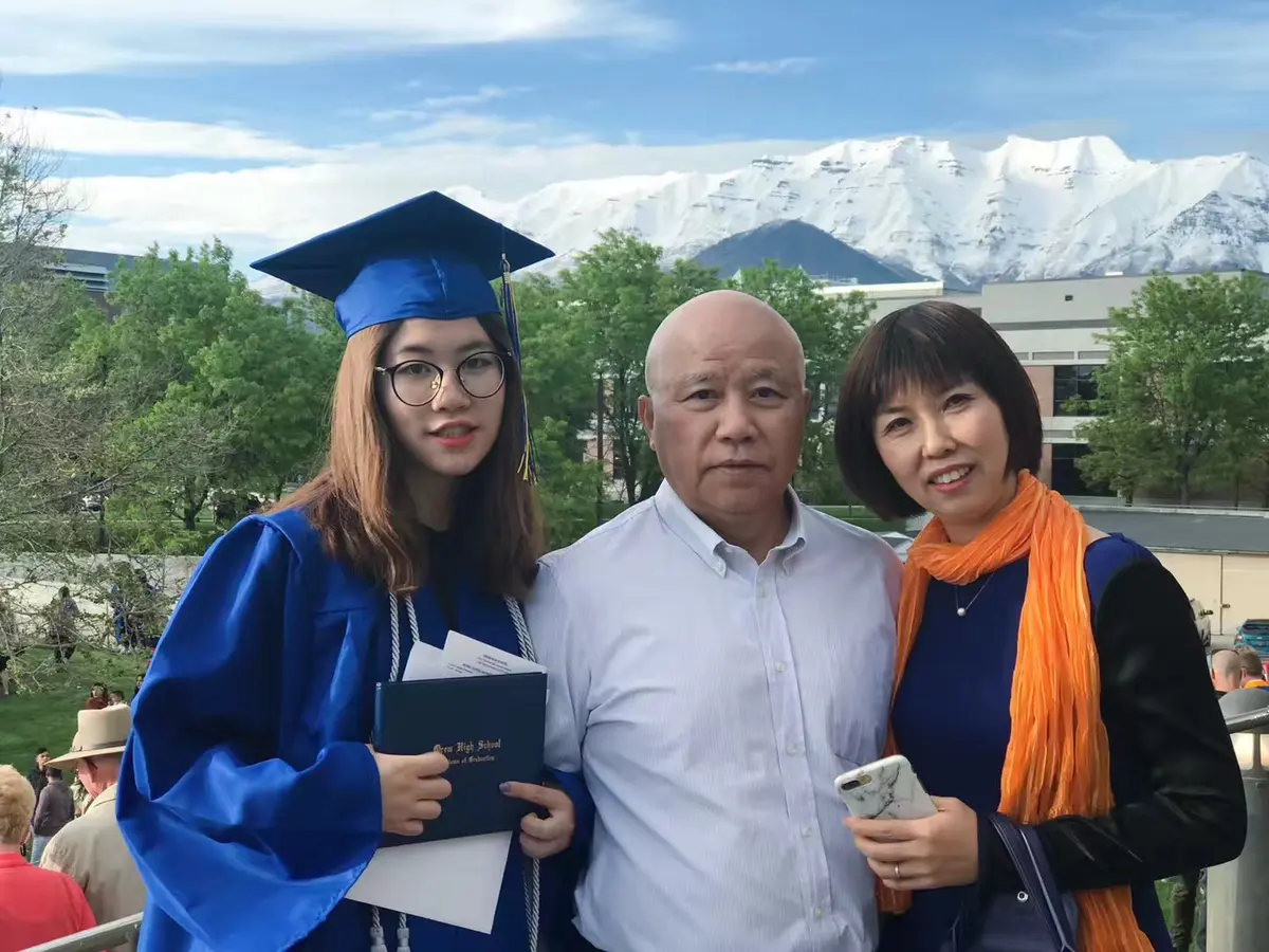 中国学生身着毕业服与家人在美国学校毕业典礼合影