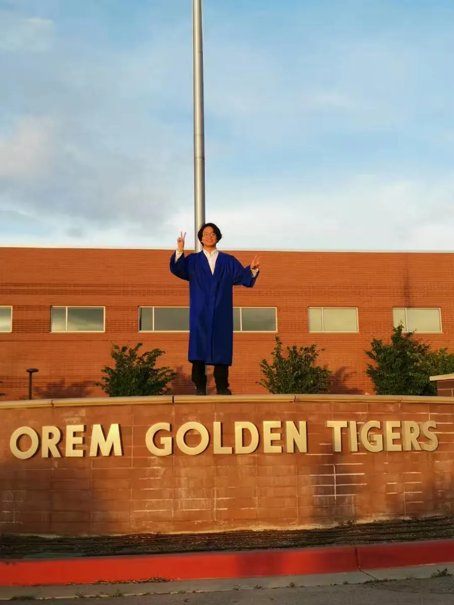 中国学生穿毕业服在 Orem High School 校名墙前庆祝毕业