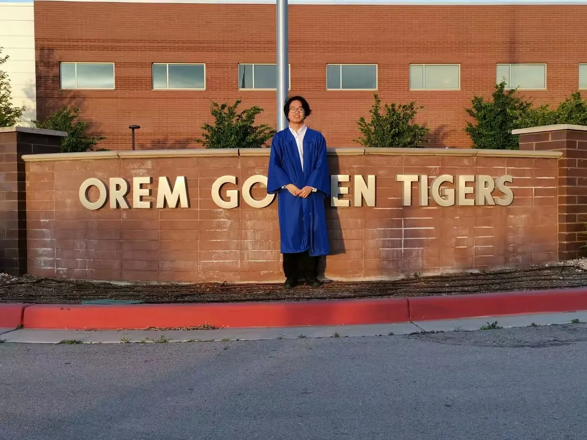 中国学生穿毕业服在 Orem High School 校名墙前留影
