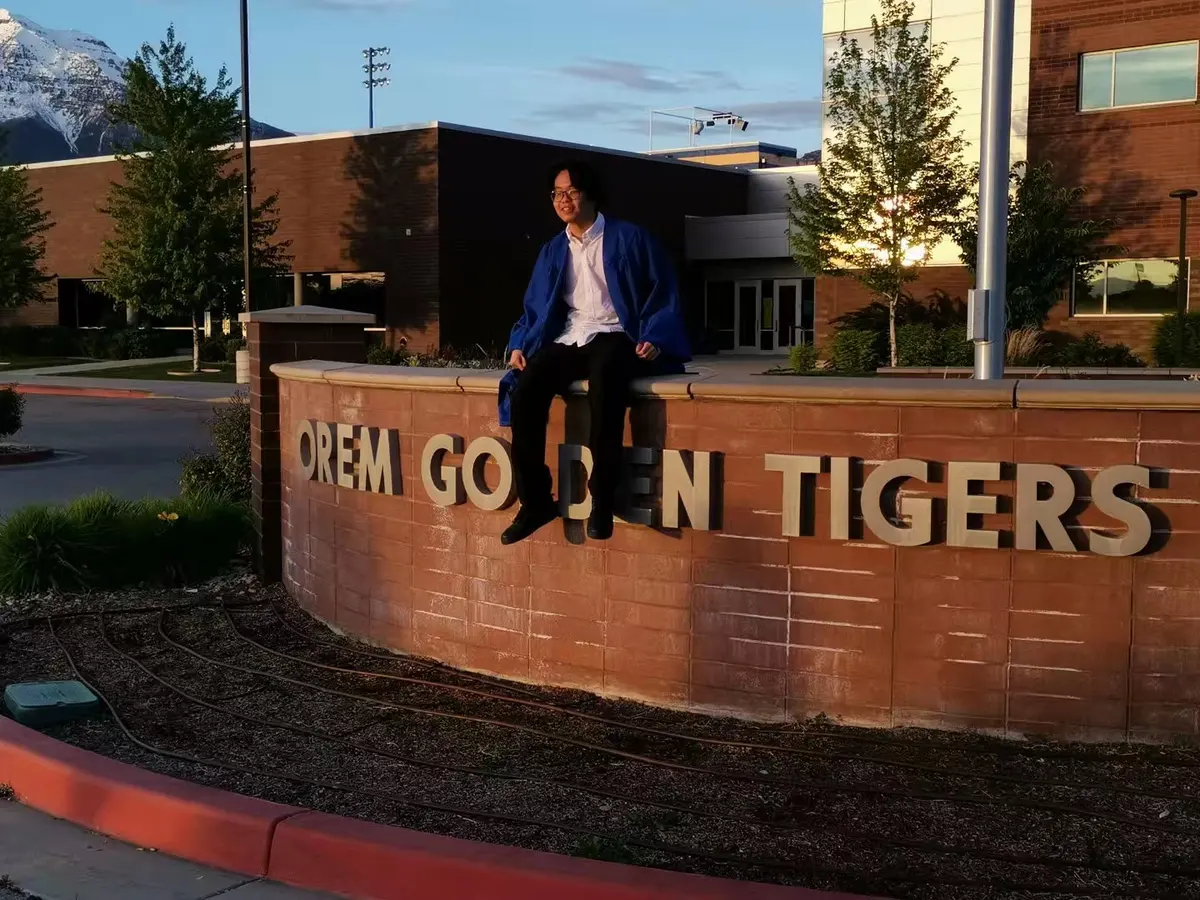 中国学生穿毕业服在 Orem High School 校名墙前留影