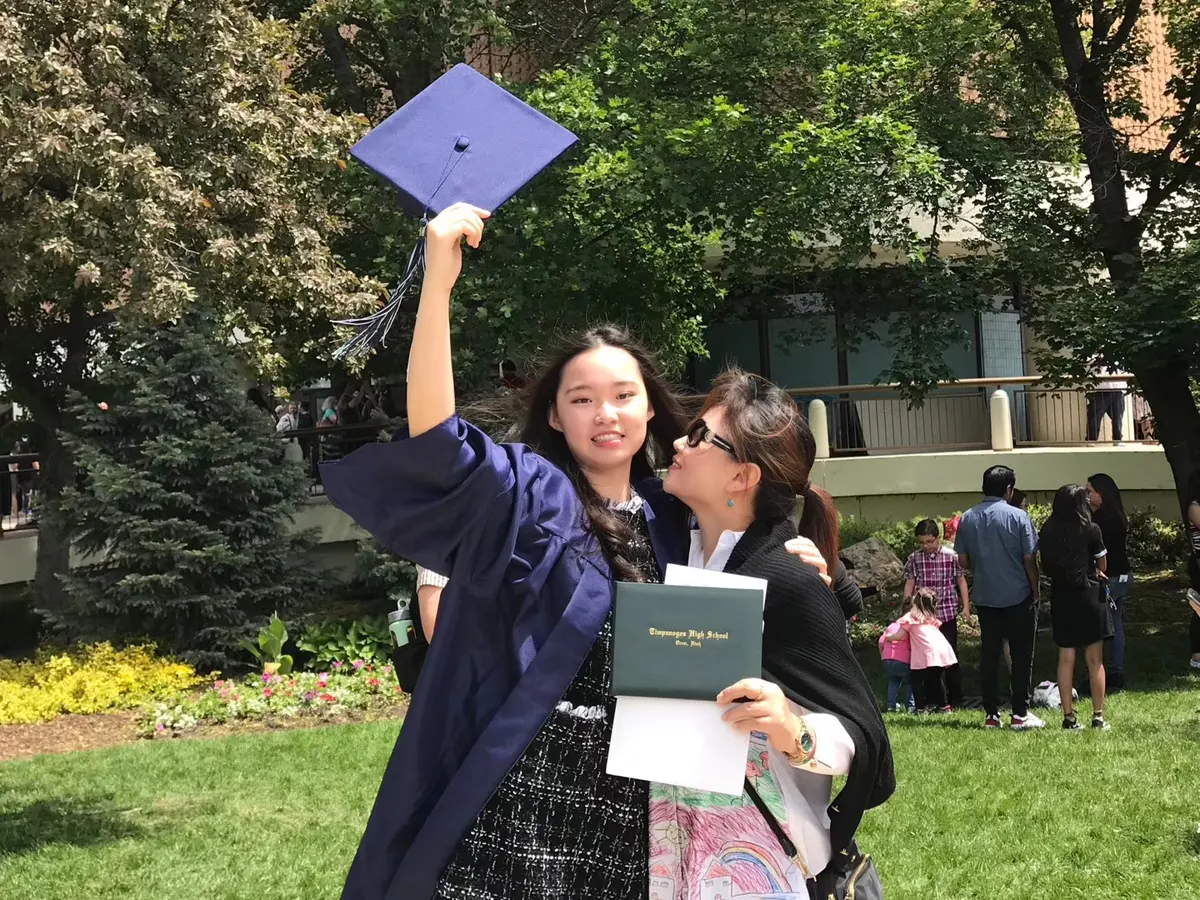 中国学生穿美国高中毕业服与同伴庆祝毕业
