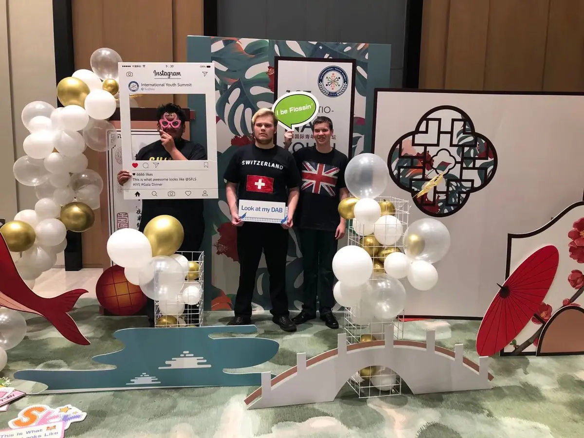 国际青年峰会参与者在主题展台前合影并展示国旗